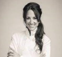B&W female chef smiling with long hair, arms crossed over white chef's jacket