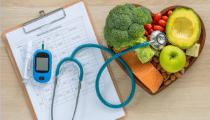 An aerial photograph of a stethoscope that has been placed on top of a clipboard and vegetables on a heart-shaped plate