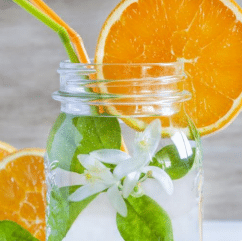 mason jar filled with water, white flowers with leaves, orange and green straws and garnished on the rim with large thin orange circle slice