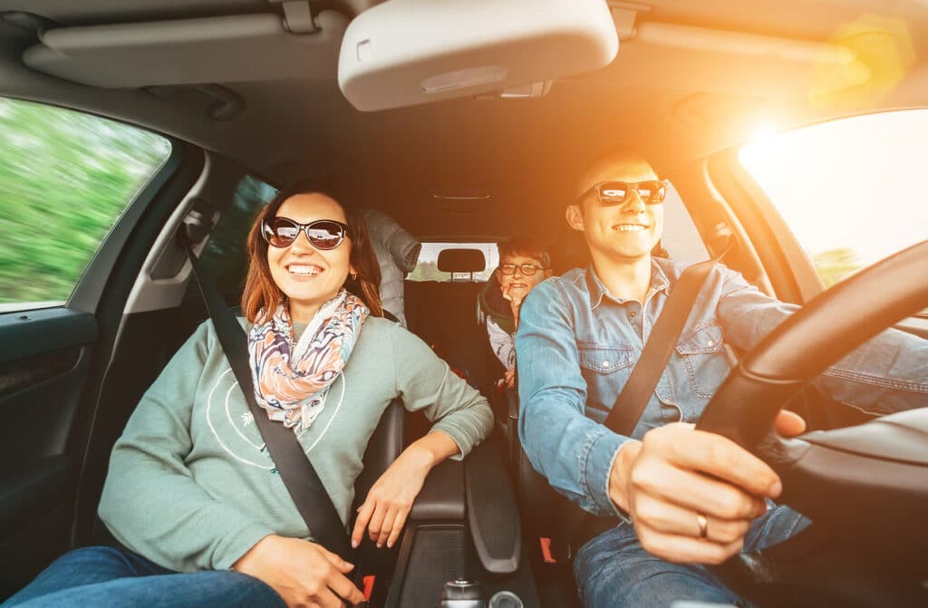 happy family traveling in car seen from windshield view on a sunny day