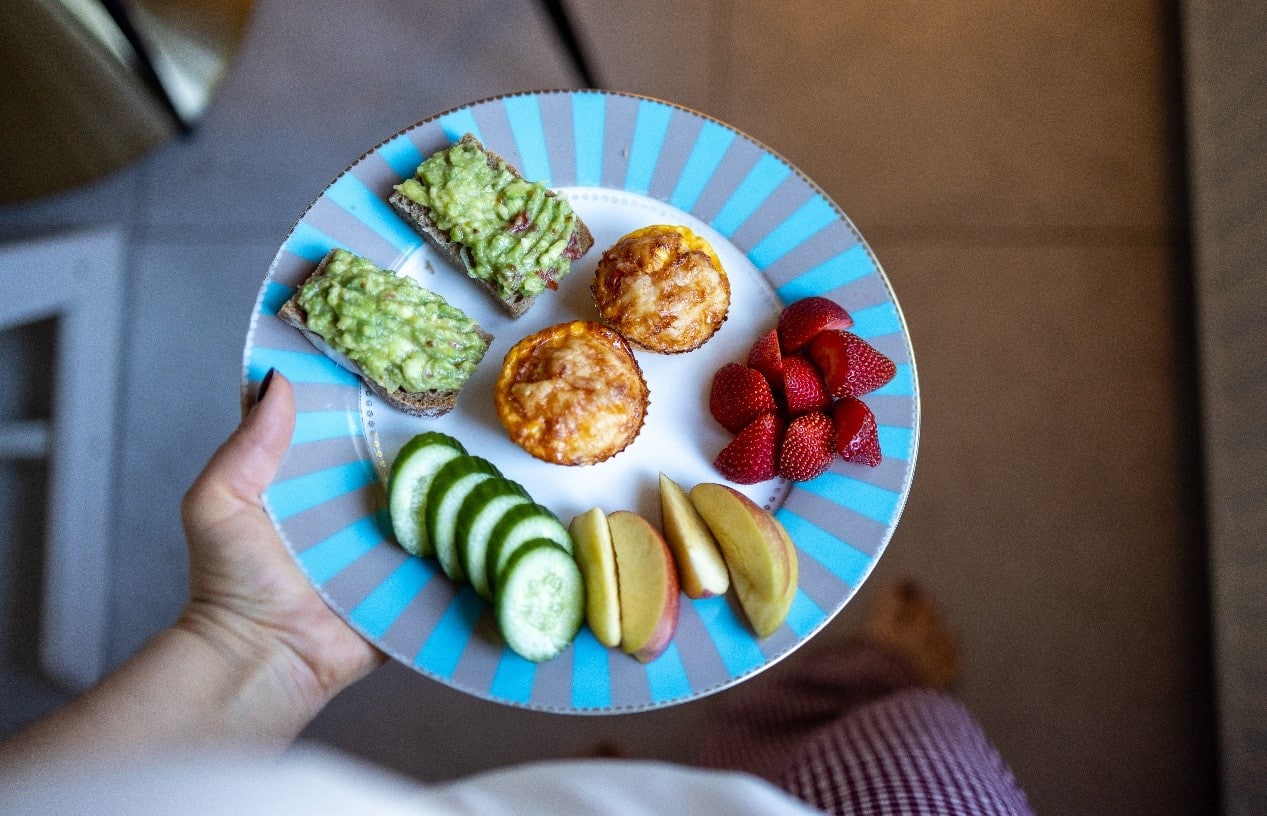breakfast plate with avocado toast, egg bites, cucumber, apple slices and strawberries on it
