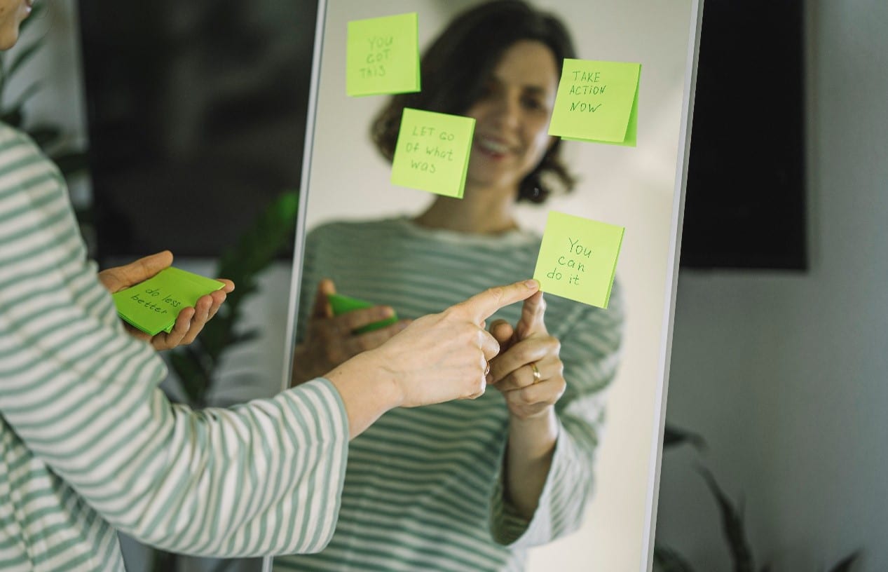 woman looking in full length mirror thru reminder post it notes scattered on it