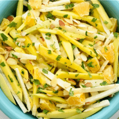 julienne-cut jicama and diced mango salad topped with green herbs in aqua bowl