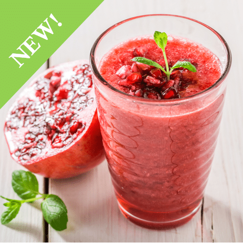 pink smoothie in glass cup with mint garnish next to a halved pomegranate